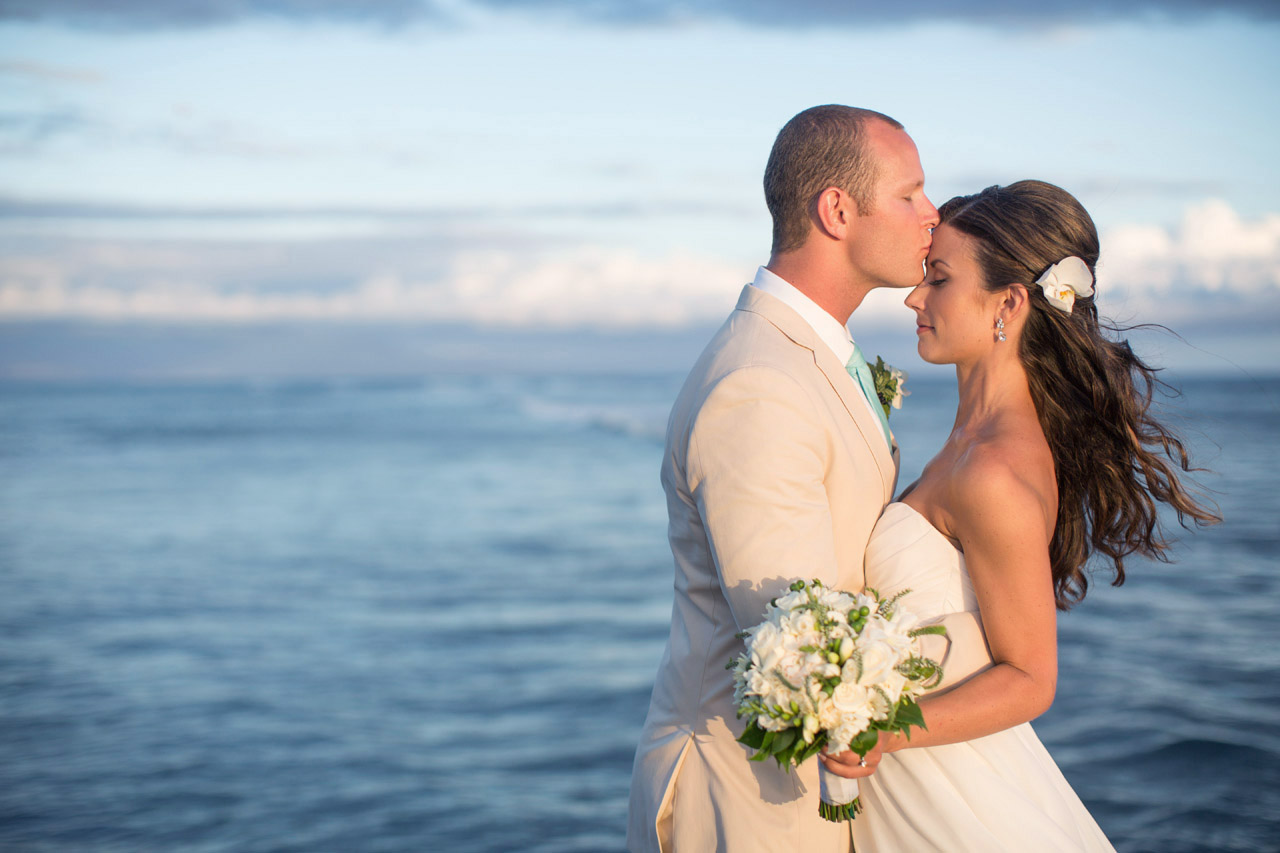 bride and groom kissing against the blue sky of maui