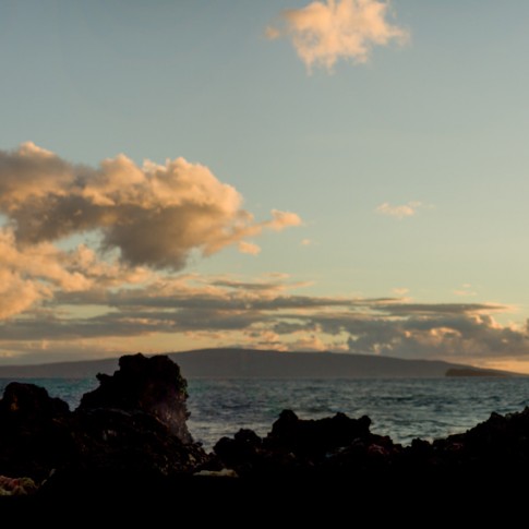 A panoramic photo of a wedding couple perched on the rocks in Wailea Maui.