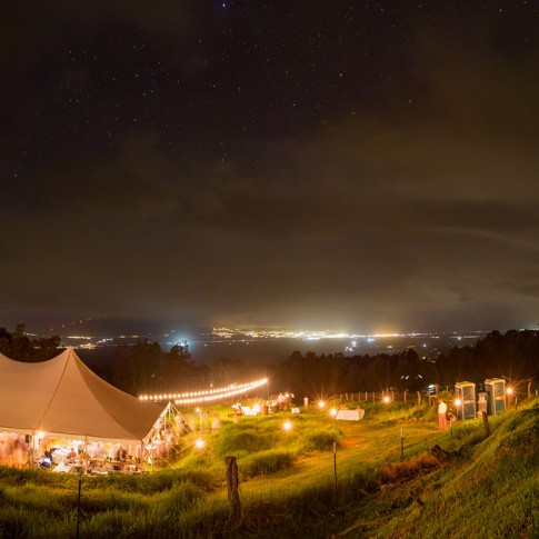 A photograph of a wedding reception glowing with the city lights of Maui in the distance.