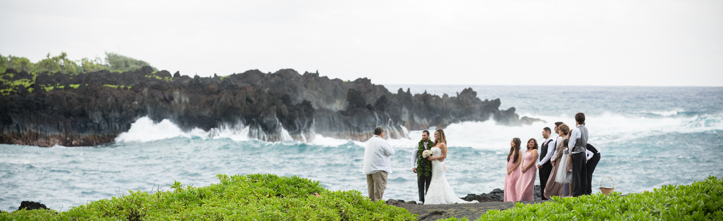A photograph of a wedding taking place set against a dramatic coastline in Hana Maui.