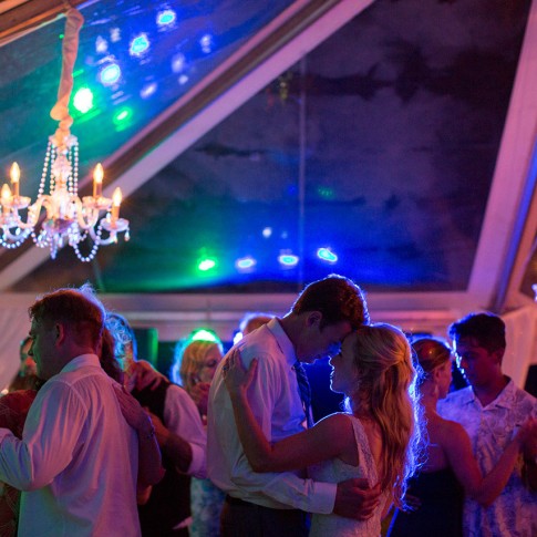 Bride and groom dance at their reception with red, blue and green lights glowing behind them.