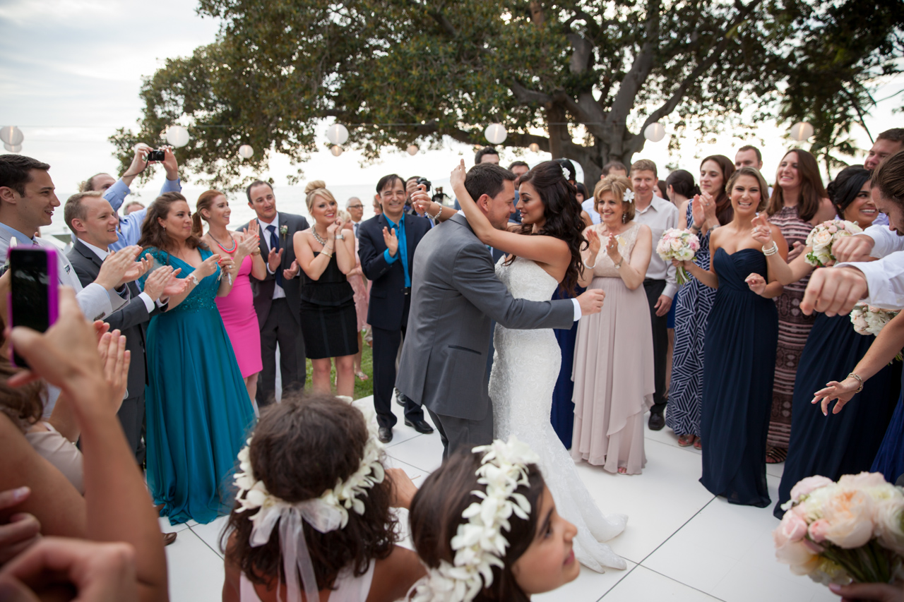 A couple dance at their wedding reception while family and friends surround them with smiles and cheers.