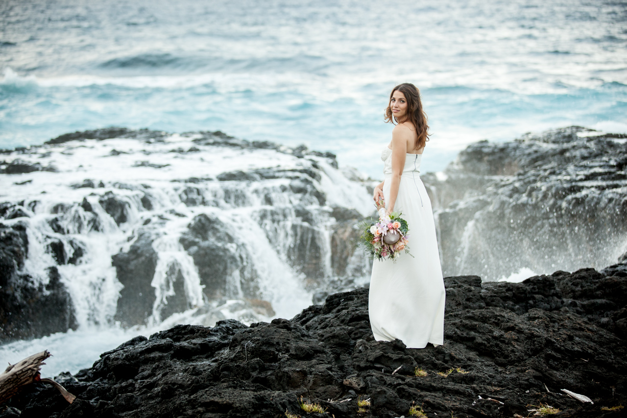 A photo of a beautiful bride in hana maui with floral bouquet against sea cliff.