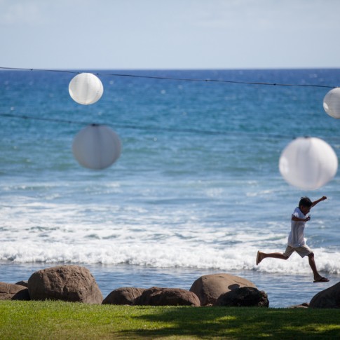 A young wedding guest jumps between rocks on the beach in Hawaii.