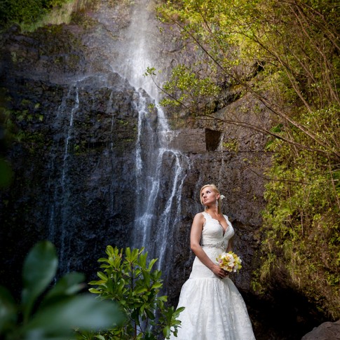 A bride poses for a photo beneath a waterfall in Hana, Maui.