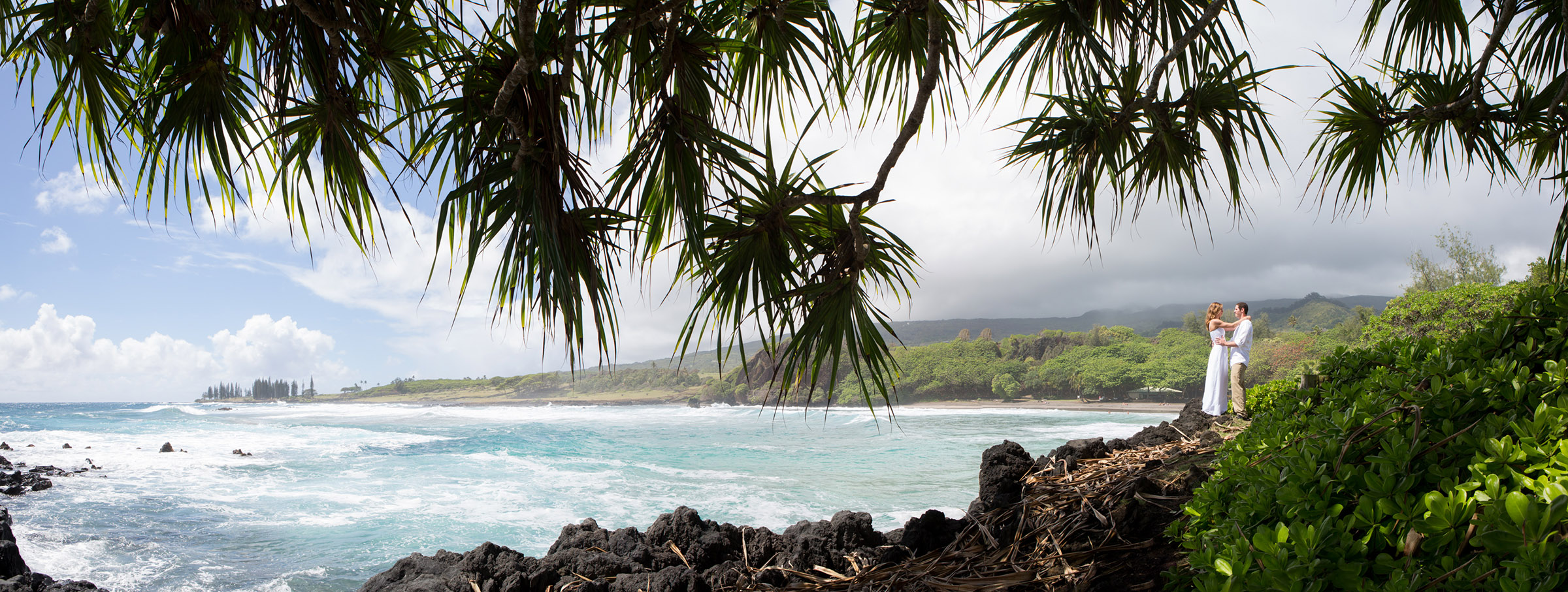 A destination wedding couple hold hands in a panoramic picture at Hamoa Beach in Hana, Hawaii.