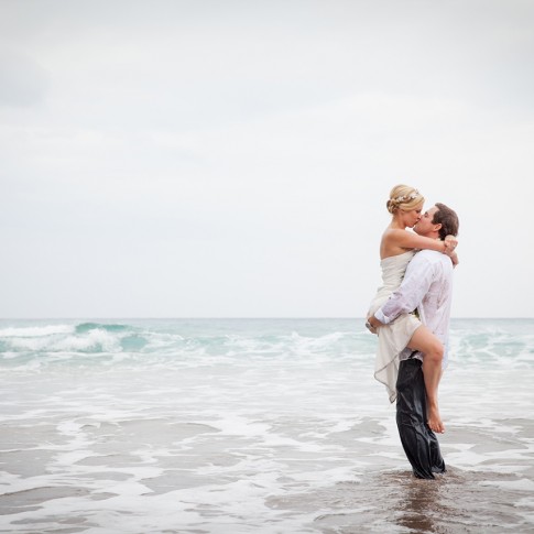 A bride clutches her husband in the ocean of Maui