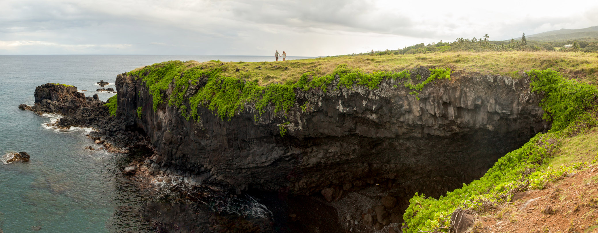 A bride stands alone on the edge of a cliff set against the blue ocean at a destination wedding in Hana Maui.