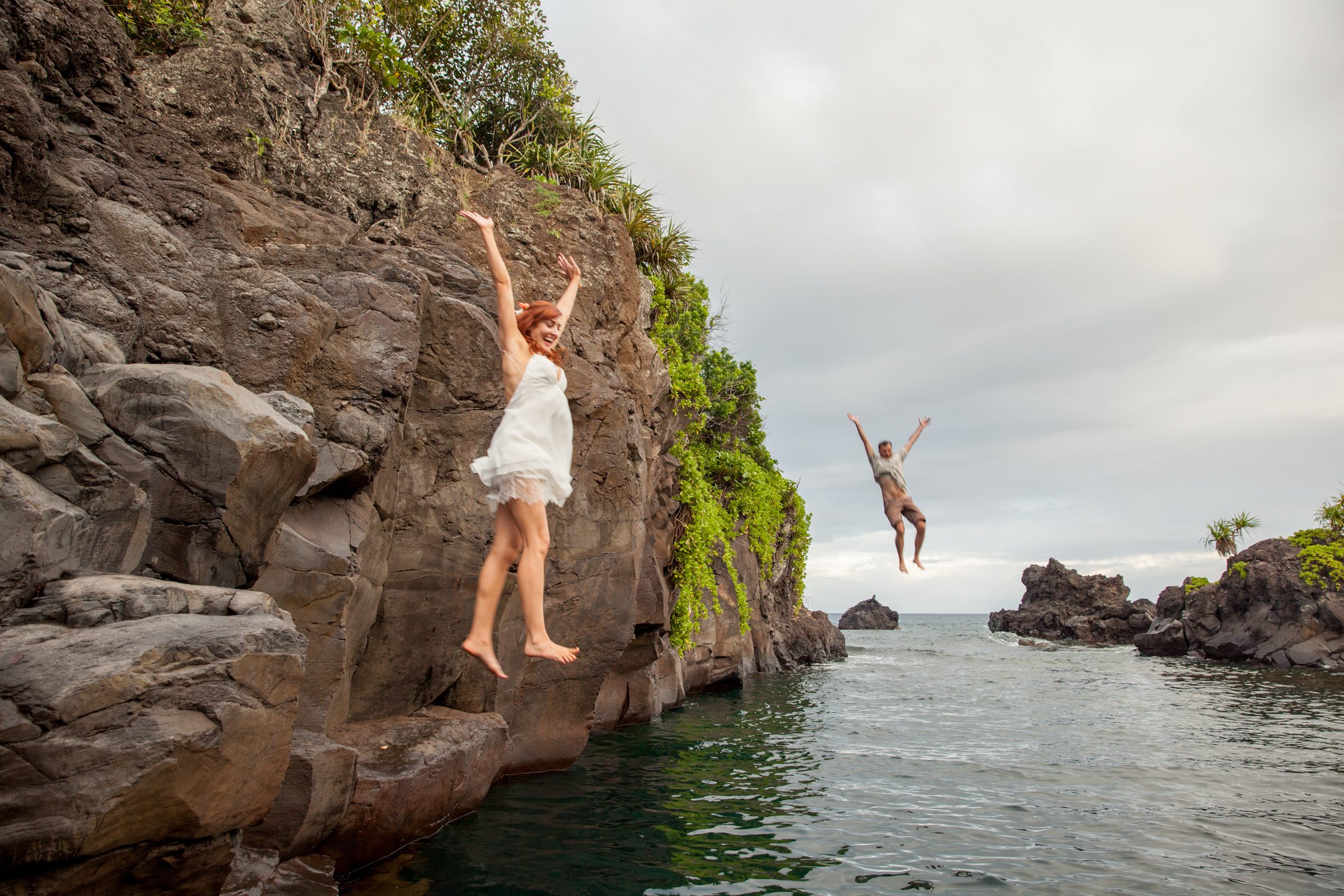 A newly wed couple literally take the plunge a jump simultaneously off a cliff into the ocean.