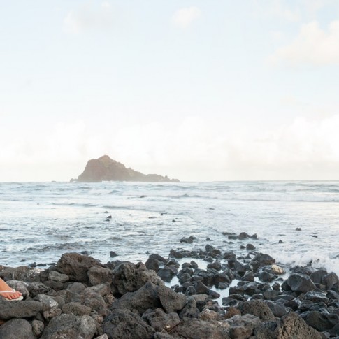 A new bride and groom sit on the rocks in hana, Maui with Alau Island in the background.