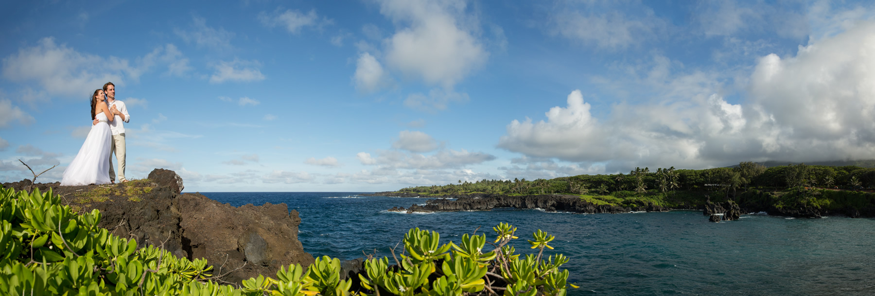 A bride and groom pose on a cliff over a dramatic sea in Hana, Maui.