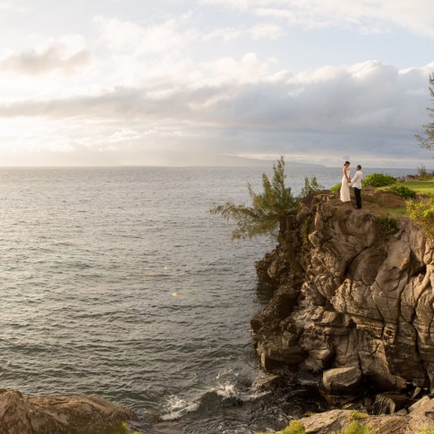 A couple hold hands while perched on a cliff in Kapalua Maui.