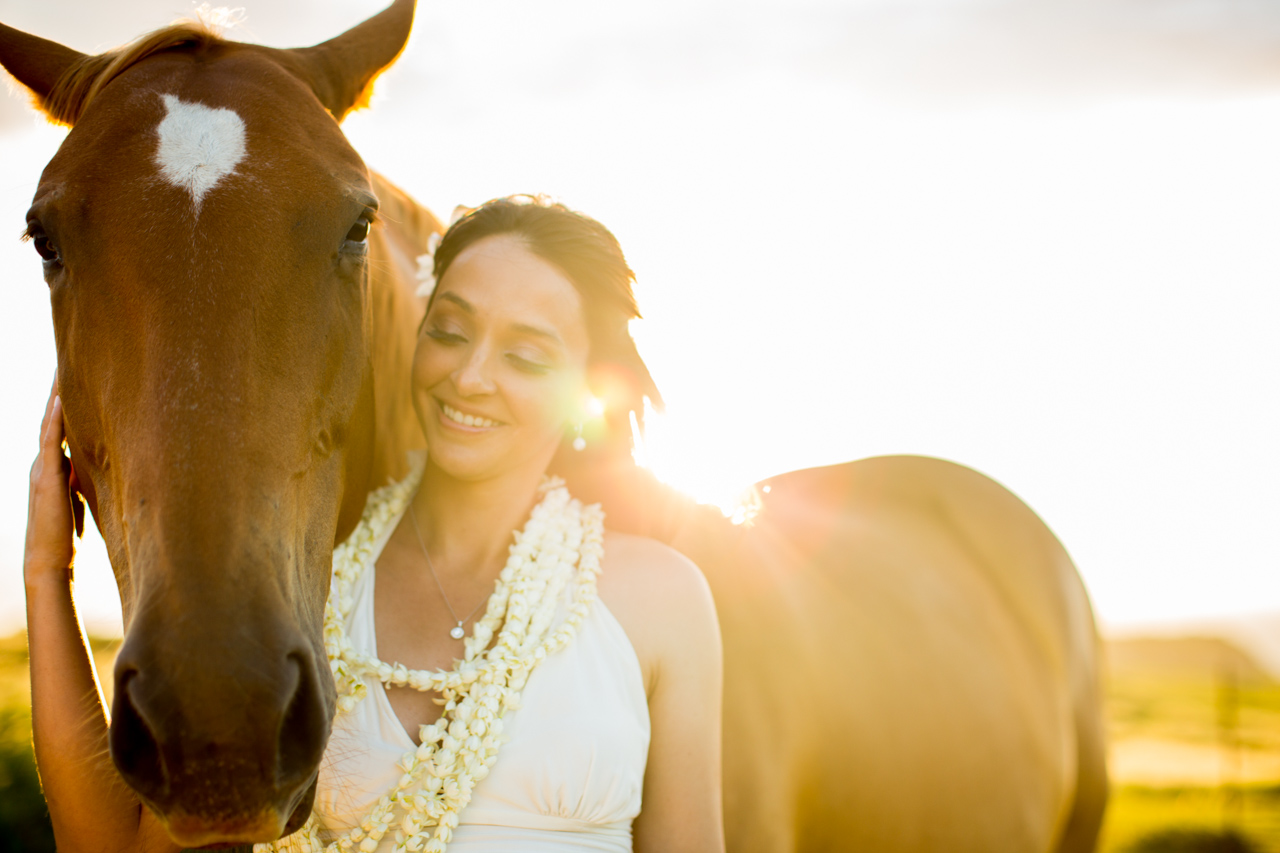bride smiling while holding a horse in the afternoon golden light in hawaii
