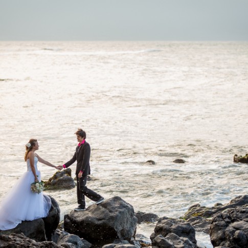image of a wedding couple standing on rocks along the waters edge while holding hands