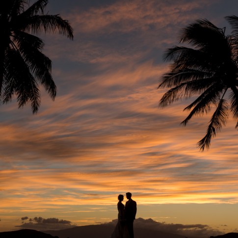 sihouette of a bride and groom and coconut pals against a dramatic red sunset