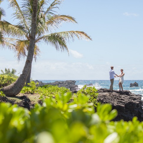a wedding couple hold hands along a tropical lava coastline in hana maui