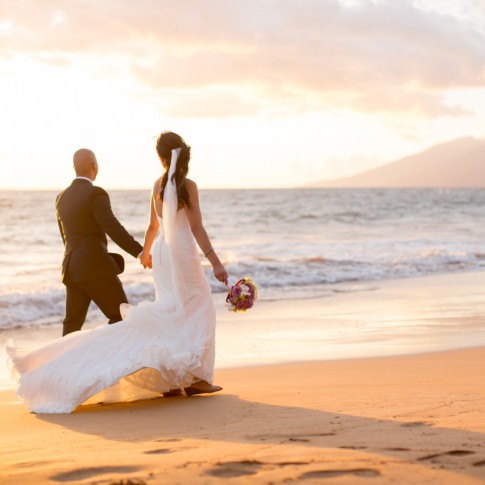 a photograph of a bride and groom walking along the sand in makena maui