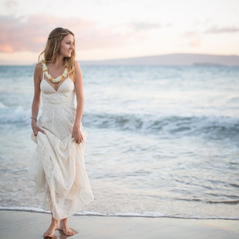 a bride stands along the edge of the ocean in her wedding dress