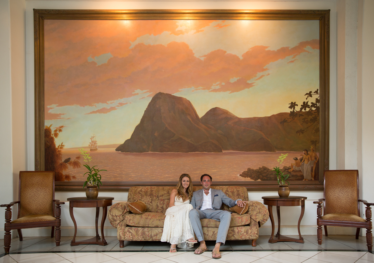 a couple sit in front of a large mural depicting the arrival of a ship to hawaii