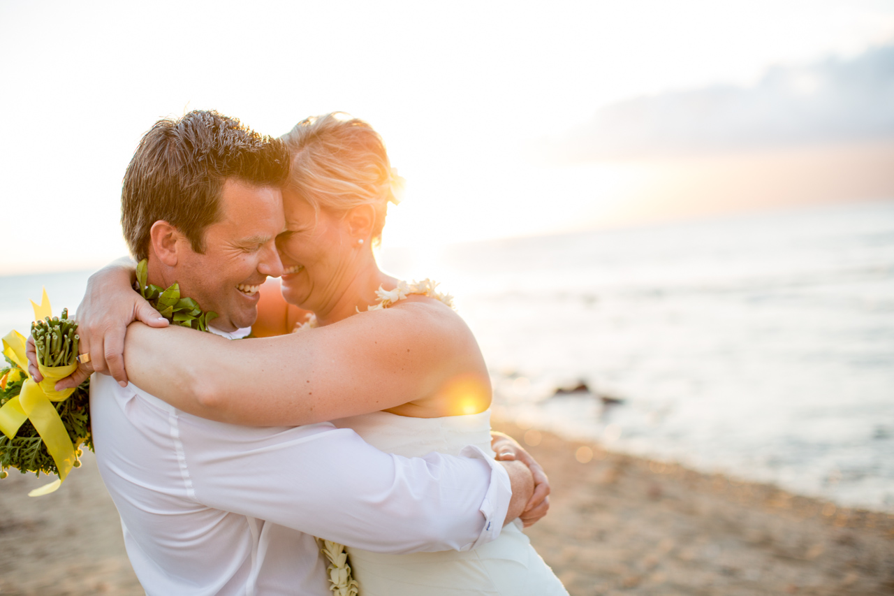 couple hugging on beach wedding in maui hawaii with sunset and floral bouquet