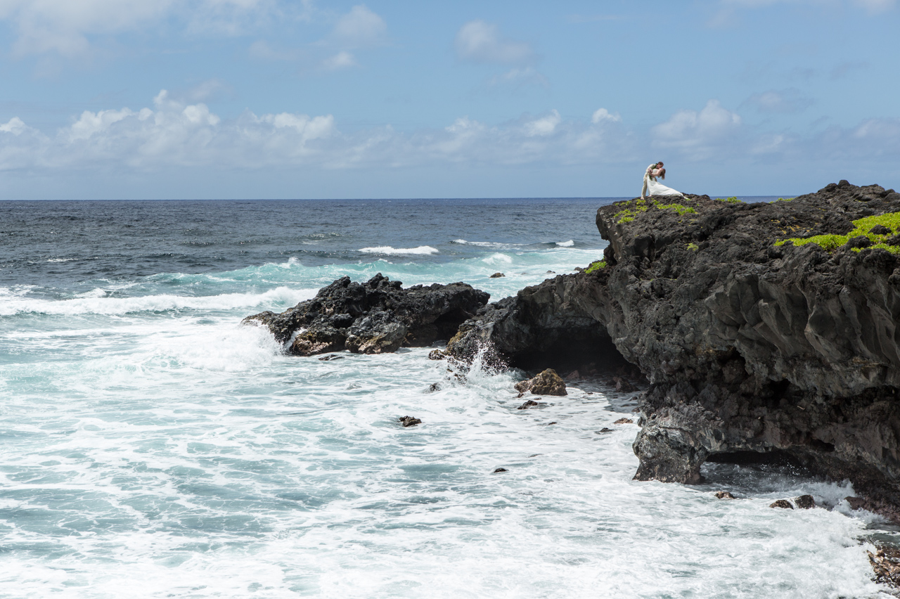 A couple embrace on a cliff set agaings the hawaiian waters