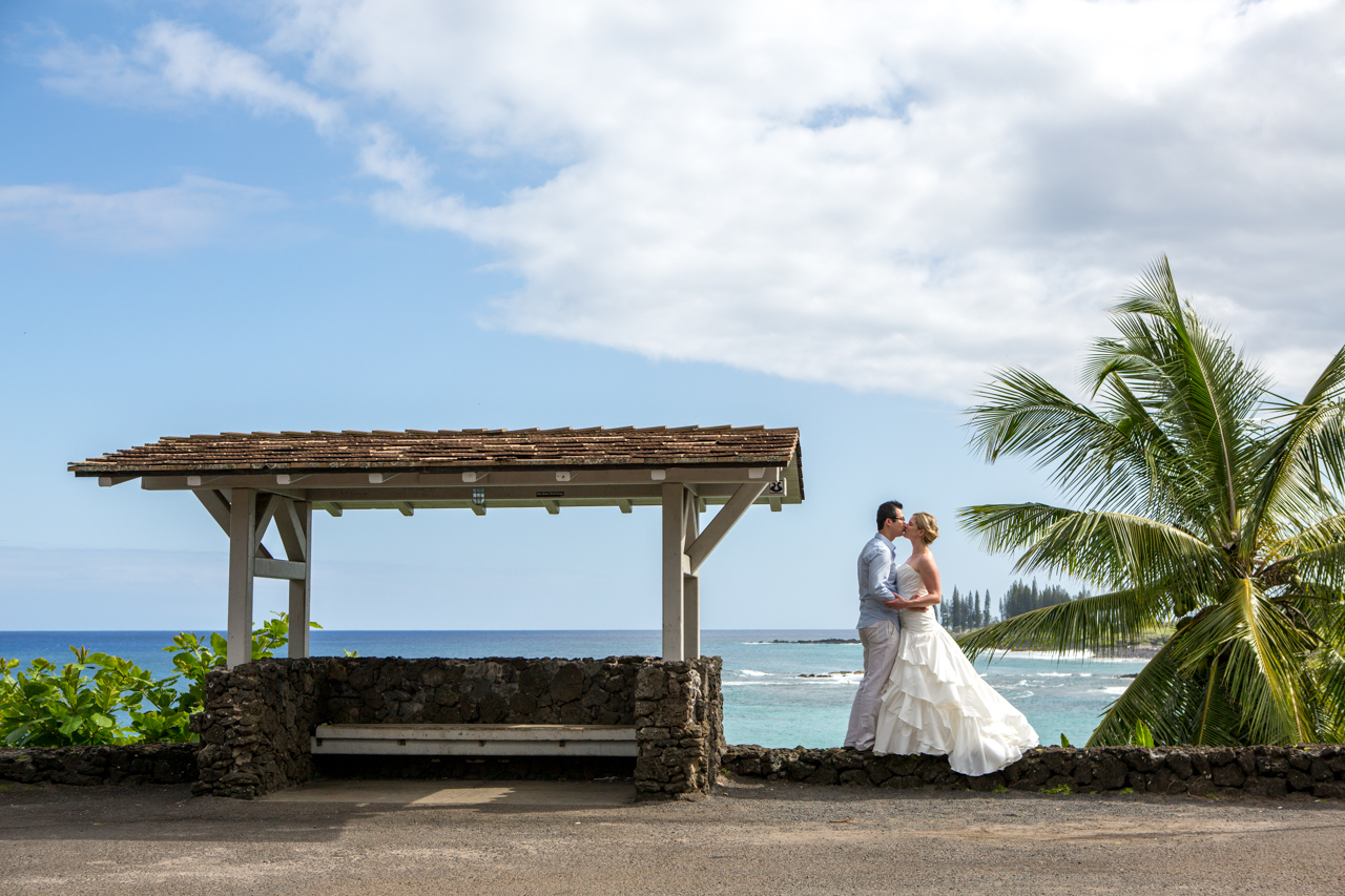 A newly married couple kissing on a rock wall at Hamoa Beach, Hana, Maui.