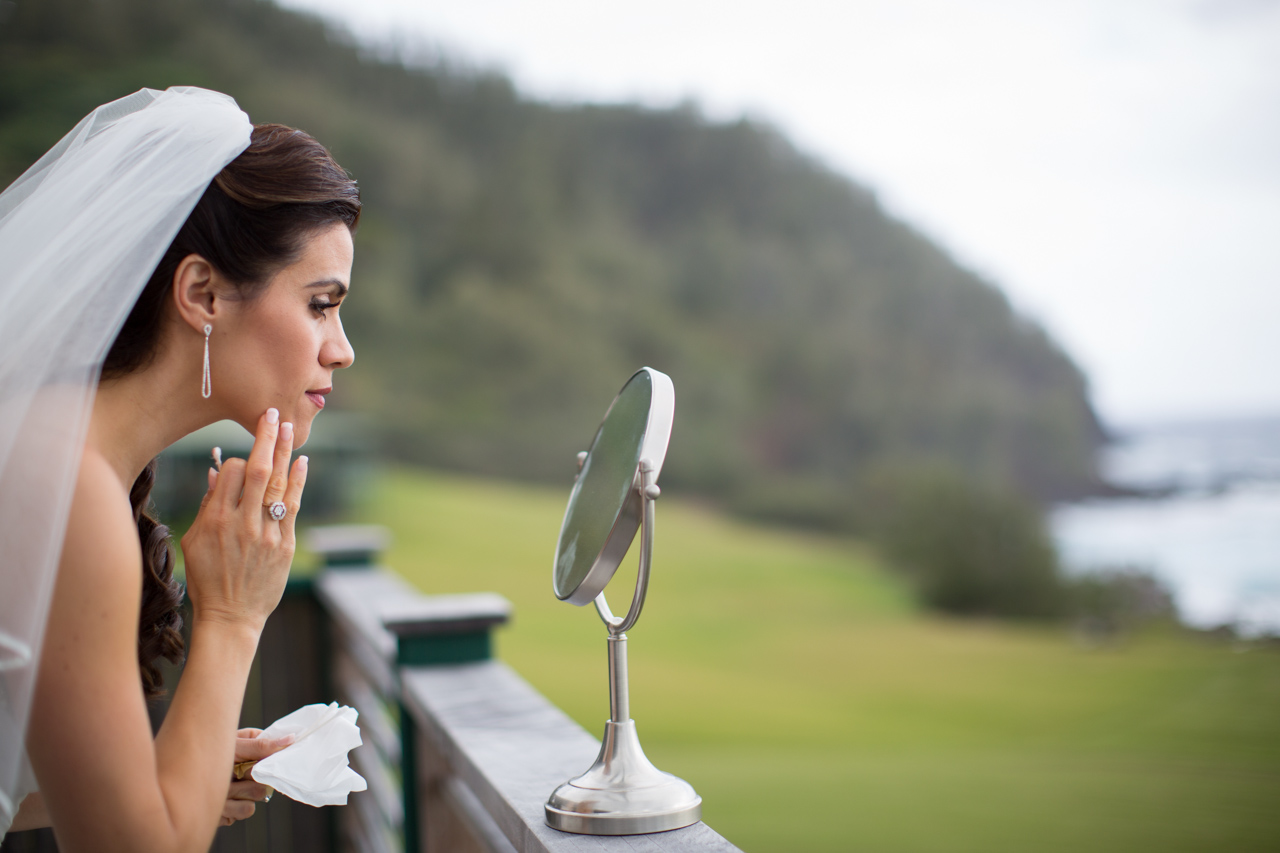 Picture of a bride checking her make-up in a mirror on the railing of her hotel balcony in Hana, Maui.