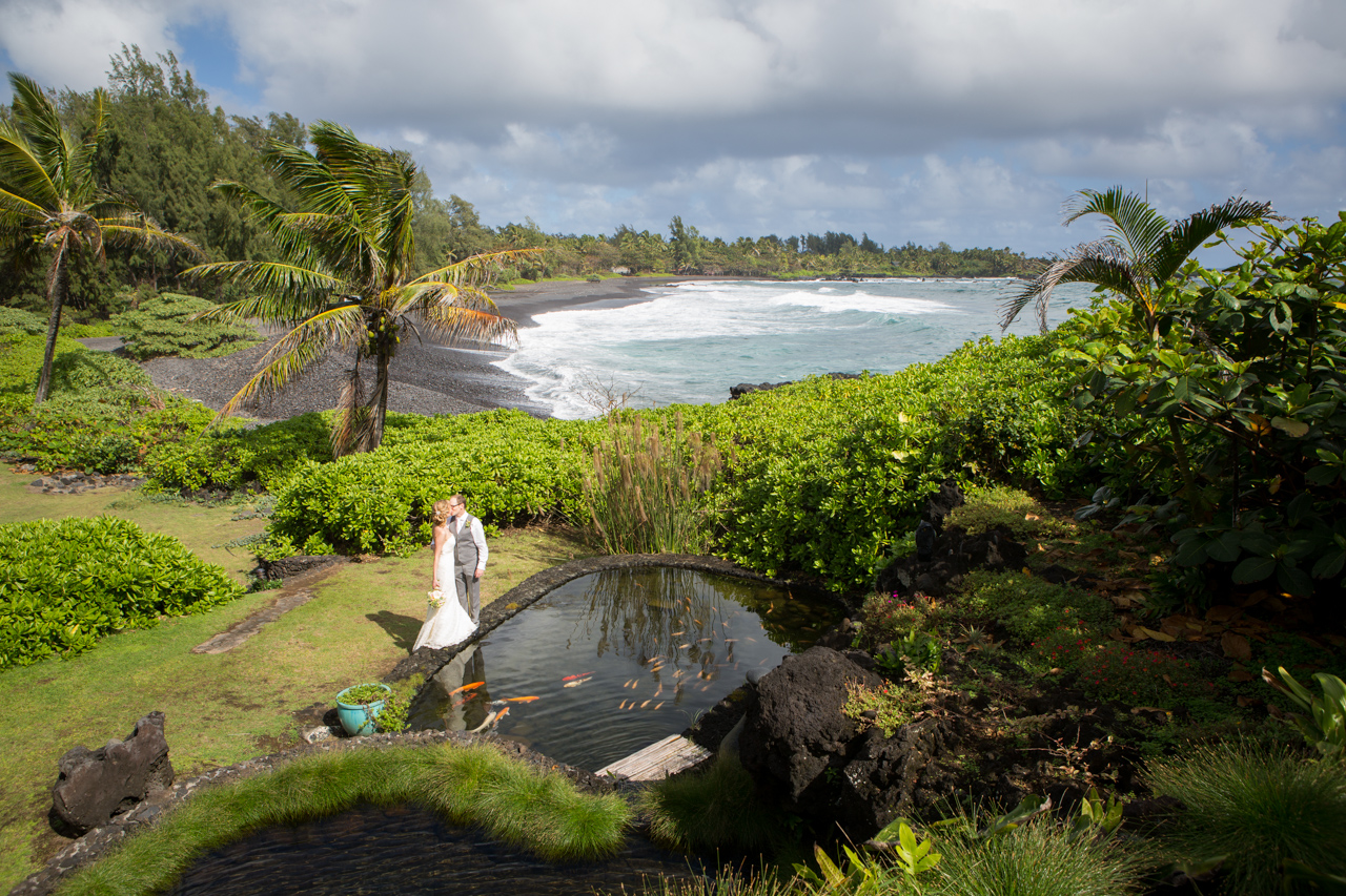 Bride and groom kiss while over looking a koi fish pond on the shores of Hana Maui