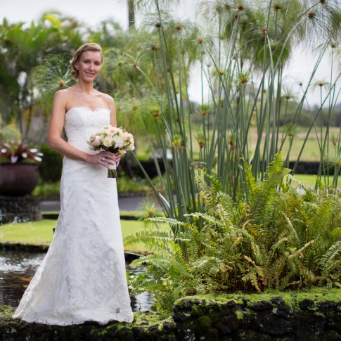 Bride standing on the edge of a koi fish pond holding her bouquet in Hana Maui