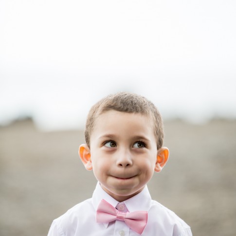 LIttle boy at a wedding wearing pink bow tie looking to his left.